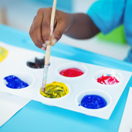 Childs hand dipping a brush into a paint palette