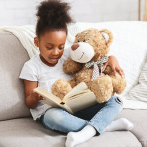 A young girl reading to a teddy bear