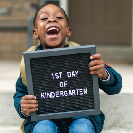 Boy holding board that reads 1st day of kindergarten